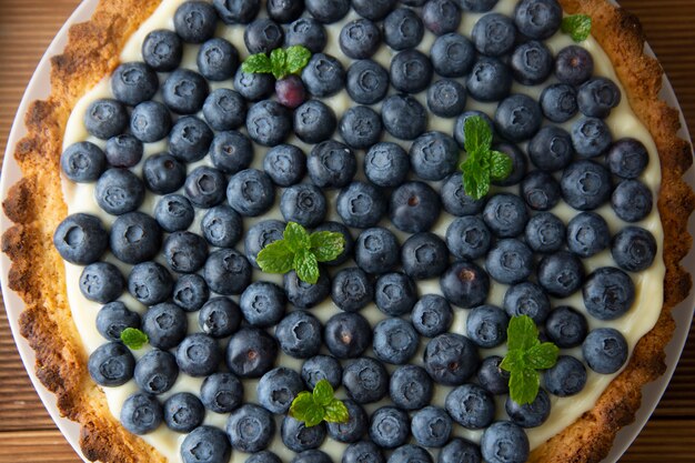 Crostata ai mirtilli o torta con panna e frutti di bosco. Cibo fatto in casa, legno, fondo rustico.