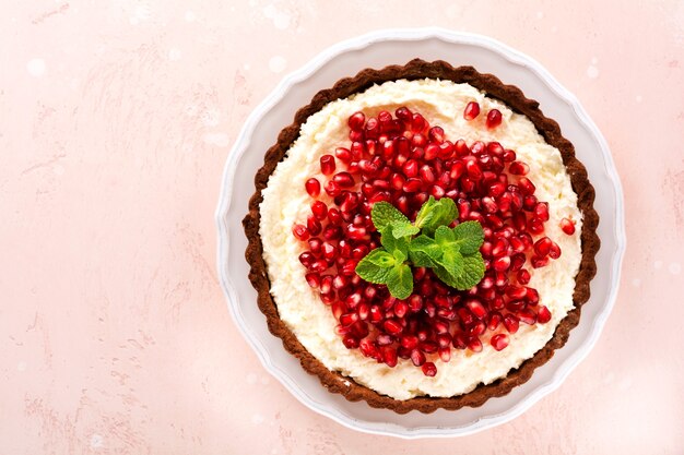 Crostata al cioccolato da dessert fatta in casa con crema di cocco e melograno e menta su uno sfondo rosa da tavola. Vista dall'alto