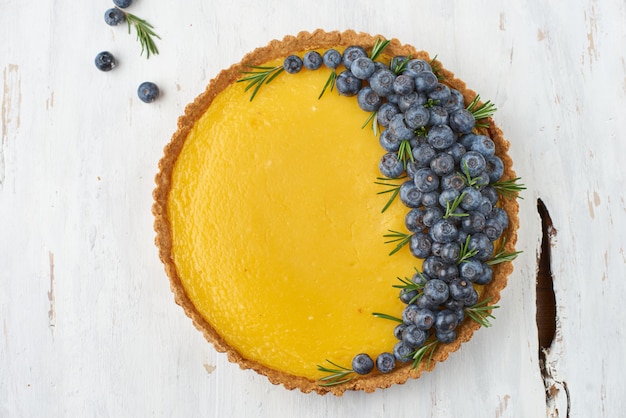 crostata con cagliata di limone e mirtilli freschi su una superficie di legno chiaro.