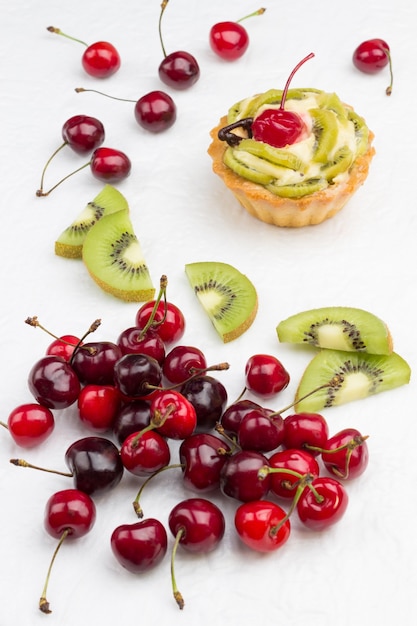 Crostata decorata con ciliegia rossa e kiwi. Kiwi e ciliegia rossa sulla superficie bianca. Vista dall'alto. Copia spazio.