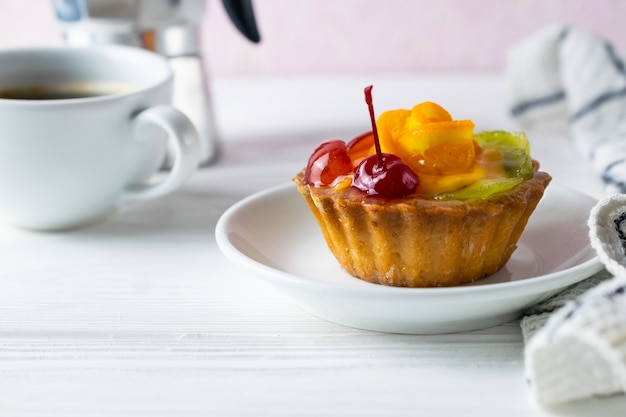 Crostata di frutta fatta in casa con arancia kiwi e ciliegia sul piatto bianco con caffè nero