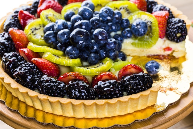 Crostata di frutta fresca su supporto per torta su tavola di legno.