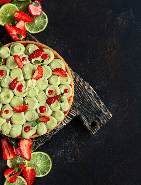 Crostata di frutta rotonda con fragole. pistacchi e lime sul tagliere di legno