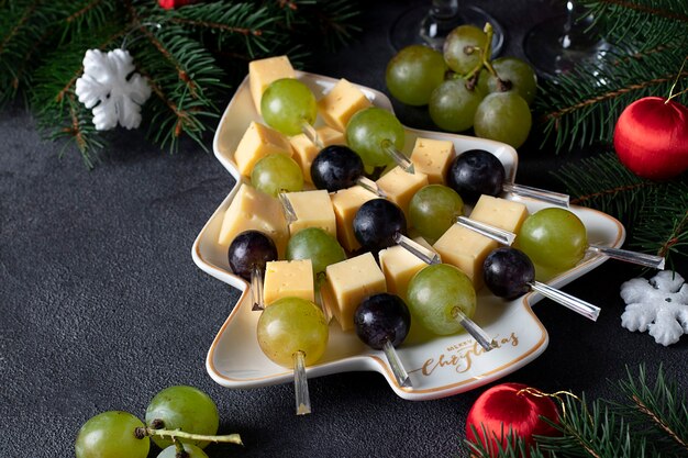 Crostini con formaggio e uva serviti nel piatto come albero di Natale, su sfondo grigio scuro. Spuntino per la festa di Capodanno