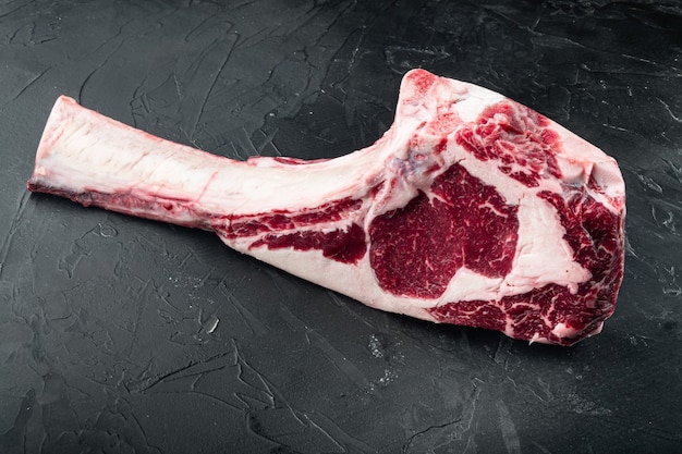 crudo fresco tomahawk secco invecchiato in marmo di manzo braciola set di bistecca, su pietra nera sfondo