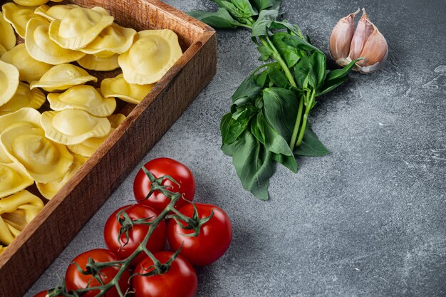 Crudo italiano ravioli fatti a mano con ingredienti freschi, basilico, pesto, prosciutto, mozzarella, parmigiano, in una scatola di legno, sul tavolo grigio