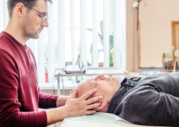 Cst terapeuta utilizza un tocco delicato per palpare le articolazioni sinartrodiali del cranio di un paziente di sesso maschile osteopatia e terapia manuale