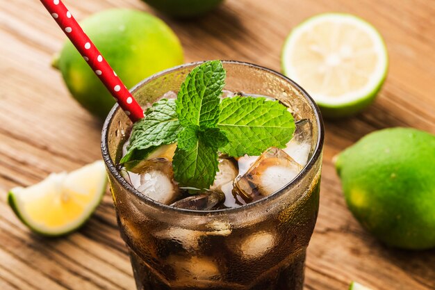 Cuba Libre fatta fresca con rum marrone, cola, menta e limone su superficie di legno