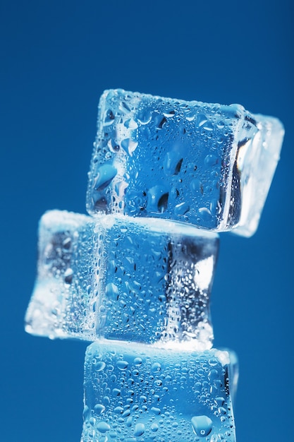 Cubetti di ghiaccio con gocce d'acqua torreggiano in fila su uno sfondo blu