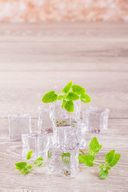 Cubetti di ghiaccio e foglie di menta di fusione in goccioline di acqua su una tabella di legno