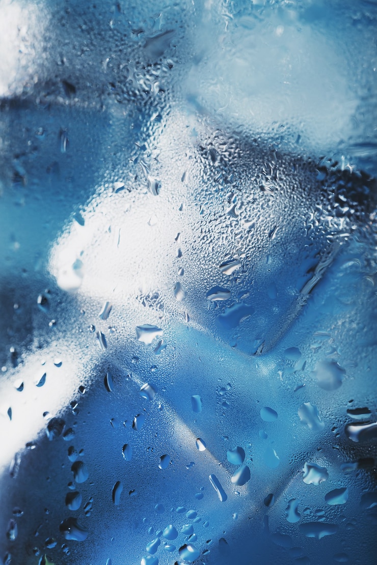 Foto cubetti di ghiaccio in un bicchiere con acqua ghiacciata rinfrescante su sfondo blu