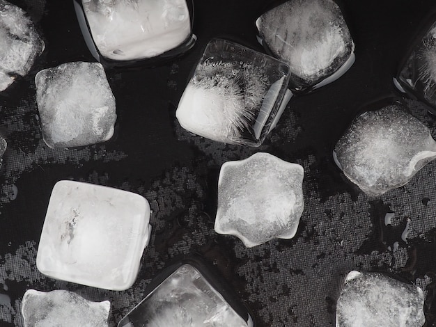 Cubetti di ghiaccio sul fondo nero della tavola con le gocce di acqua.