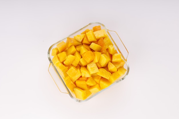 Cubetti di mango maturi o pezzi tagliati disposti in un contenitore quadrato di vetro con sfondo bianco.