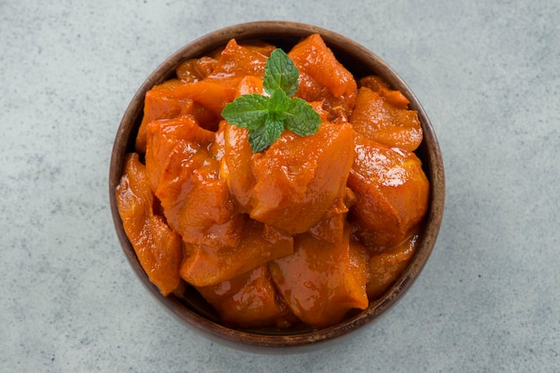 Cubetti di pollo marinati crudi disposti in stoviglie di legno guarnite con foglia di menta fresca che viene posta su uno sfondo grigio bianco testurizzato.