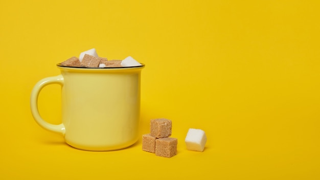 Cubetti di zucchero bianco e marrone di canna in tazza gialla su sfondo giallo spazio copia