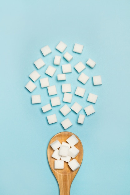 Cubetti di zucchero bianco su un cucchiaio di legno e su sfondo blu