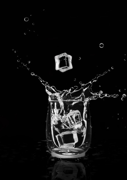 Cubetto di ghiaccio che cade in un bicchiere e spruzzi d'acqua su sfondo nero