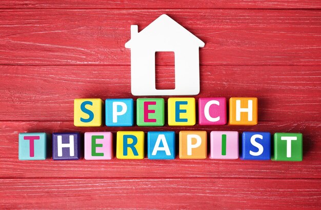 Cubi colorati con il testo SPEECH THERAPIST su sfondo di legno rosso