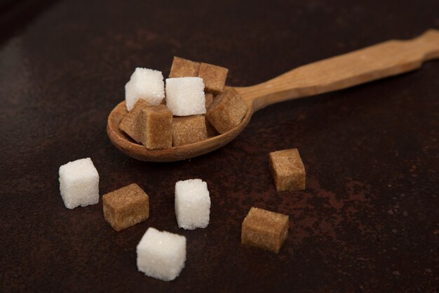 Cubi dello zucchero marrone e bianco sul cucchiaio di legno