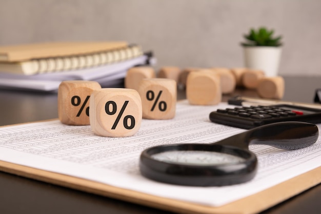 Cubi di legno che mostrano il simbolo percentuale sui documenti finanziari con una calcolatrice a ingrandimento e una pianta in vaso