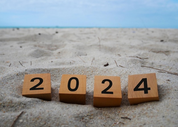 Cubi di legno con l'iscrizione "2024" e "Buon anno nuovo" sullo sfondo della sabbia della spiaggia