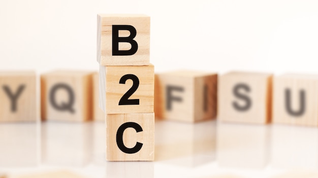 Cubi di legno con lettere B2C disposti in una piramide verticale, sfondo bianco, riflesso dalla superficie del tavolo, concetto di business. b2c - abbreviazione di business to consumer