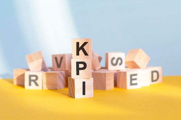 Cubi di legno con lettere KPI disposti in una piramide verticale, sfondo grigio e giallo, concetto di affari. kpi - abbreviazione di indicatori chiave di prestazione