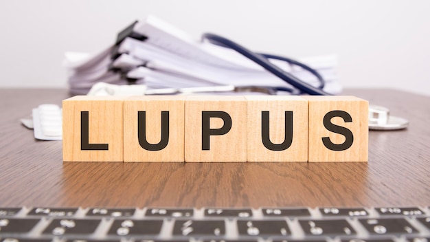 Cubi di legno formano le lettere LUPUS con stetoscopio pillole blocco appunti sul desktop del medico concetto medico