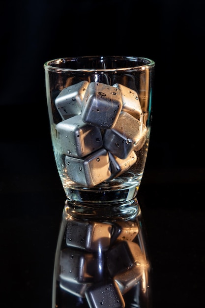 Cubi in acciaio inossidabile che simulano il ghiaccio in bicchiere di whisky su un tavolo nero