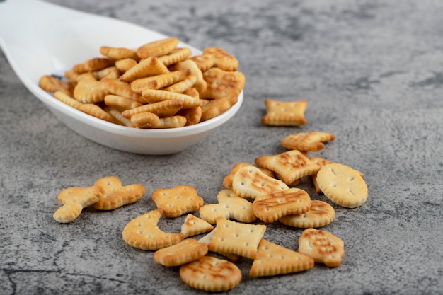 Cucchiaio bianco pieno di cracker croccanti posto su uno sfondo di pietra.