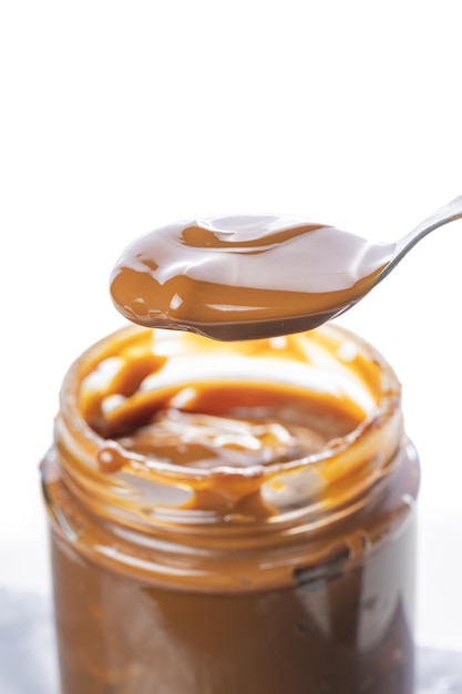 Cucchiaio che raccoglie dulce de leche da un barattolo dolce tradizionale dall'Argentina isolato su sfondo bianco