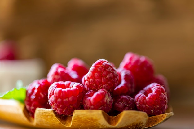 Cucchiaio con lampone e ciotola con marmellata di lamponi su fondo di legno,