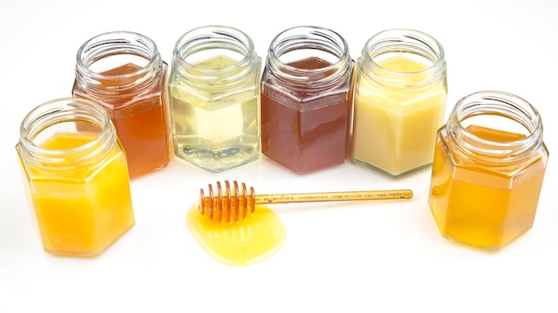 Cucchiaio con miele fresco e vasetti con diversi tipi di miele su sfondo bianco alimenti vitaminici organici