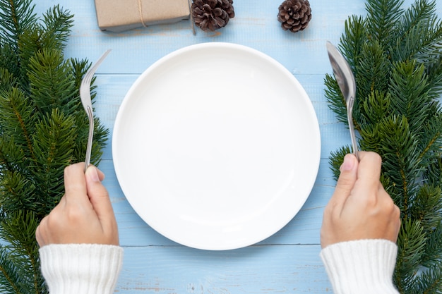 Cucchiaio della holding della mano della donna e forcella sopra Piatto vuoto con decorazione di Natale