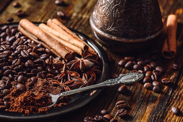 Cucchiaio di caffè macinato, chicchi di caffè e alcune spezie sulla piastra.