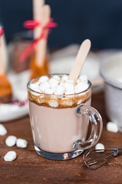 Cucchiaio di cioccolata calda al caramello salato in tazza di vetro condita con marshmallow.