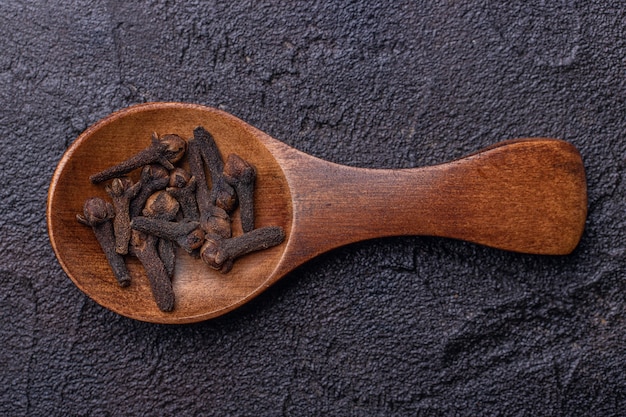 Cucchiaio di legno con chiodi di garofano su uno sfondo scuro di cemento