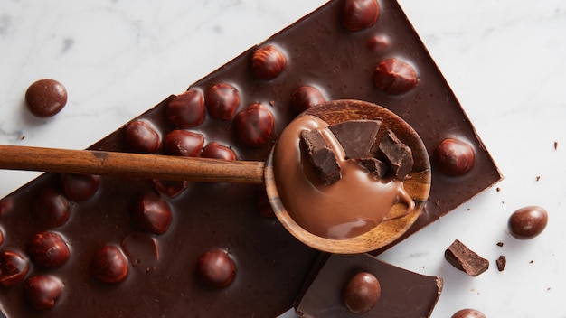 Cucchiaio di legno con cioccolato e palline di cioccolato su una superficie di marmo bianco