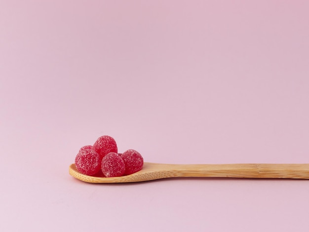 Cucchiaio di legno con fagioli di gelatina rossi su sfondo rosa vista laterale