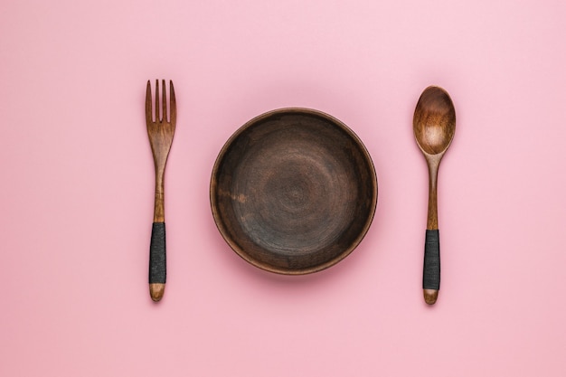 Cucchiaio di legno e forchetta e ciotola di argilla su sfondo rosa. Stoviglie d'epoca. Disposizione piatta.