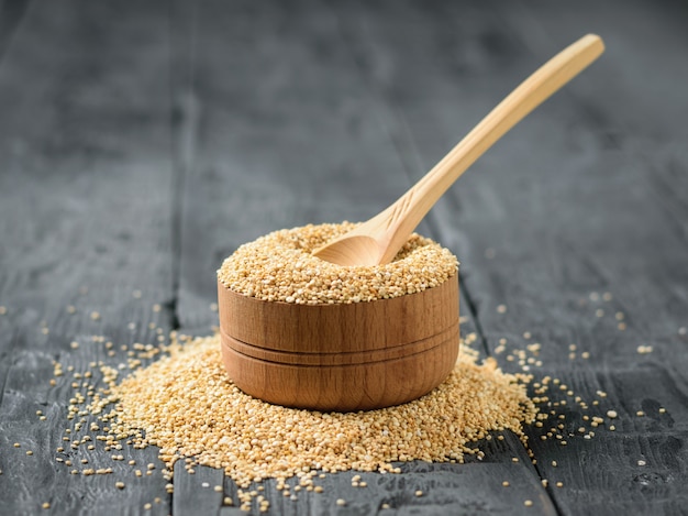 Cucchiaio di legno in legno chiaro in una ciotola di legno piena di semi di quinoa su un tavolo scuro.