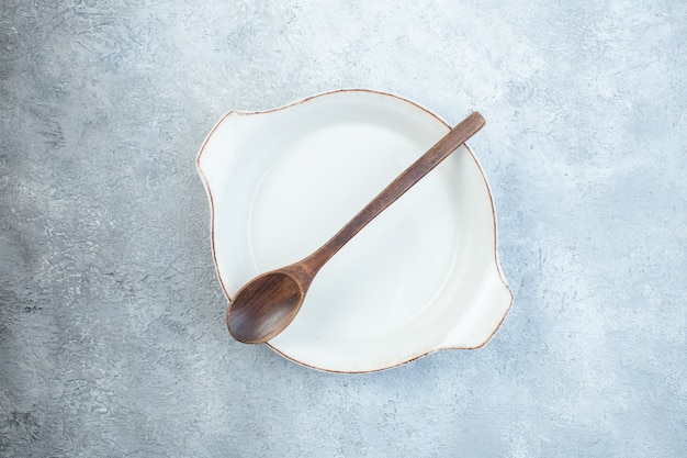 Cucchiaio di legno nel piatto vuoto bianco sulla superficie grigia