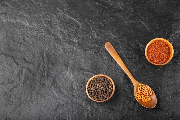 Cucchiaio di pasta cruda e spezie pepe su sfondo nero.