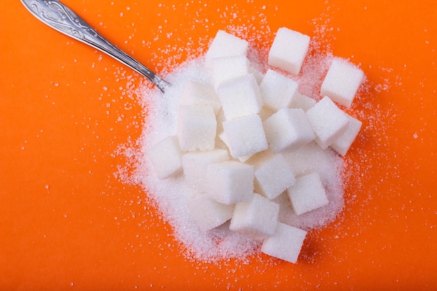 Cucchiaio e cubetti di zucchero bianco e zucchero semolato su fondo arancione