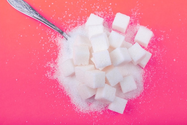 Cucchiaio e cubetti di zucchero bianco e zucchero semolato su fondo rosa