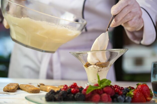 Cucchiaio mettendo la crema nei biscotti di vetro vicino ai frutti di bosco freschi come preparare il tiramisù confetture sapienti...