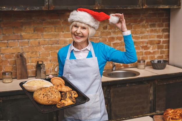 Cucina di Capodanno. Il ritratto della donna invecchiata senior attraente sta cucinando sulla cucina. Nonna che produce cottura saporita di natale.