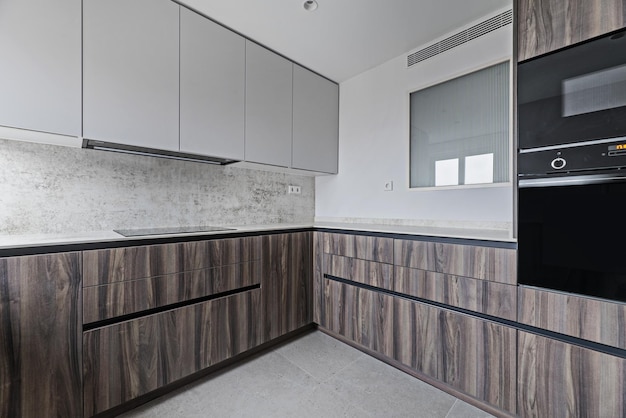 Cucina di nuova installazione dal design contemporaneo con armadi in legno di radice, elettrodomestici neri lucidi e pavimenti in piastrelle grigie