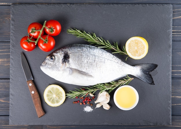 Cucina e ingredienti del dorado del pesce crudo. Dorado, limone, pomodoro, erbe aromatiche e spezie. Vista dall'alto sulla tavola di legno