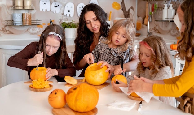 Cucina giovane madre che tiene un coltello ang scolpire faccia spaventosa su zucca in cucina bianca chiara a casa wi